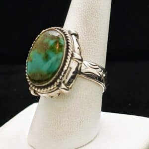 "A sterling silver ring featuring an oval blue-green Chinese turquoise cabochon with dark gold matrix, fancy bezel, and intricate carving on the band, size 9, part of the Ethnographic line by Turquoise Deluxe."